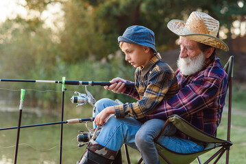 Likable respected 70-aged bearded grandfather holding on knees 10-aged cute grandson and teaching...