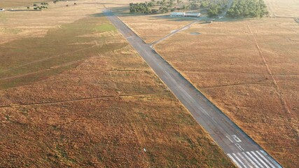 Empty runway of a small airport used for takeoff and landing of light aircraft. Airfield for general aviation and light-sport planes in the middle of a field covered with yellow grass.