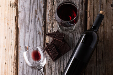 Elegant bottle and wineglasses with red wine and dark chocolate on rustic wooden background. Top...