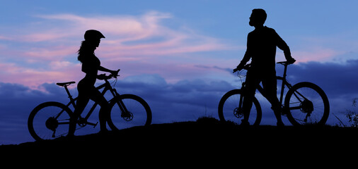 Fototapeta na wymiar Two silhouettes of cyclists on a sunset background. Athletic guy and a girl on modern mountain bikes go to each other.