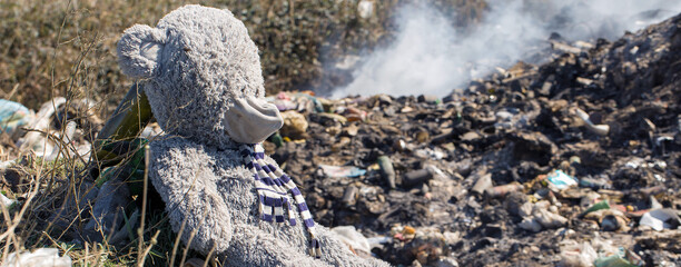 A teddy bear lies thrown away in the middle of a garbage fuming landfill. The concept of environmental disaster.