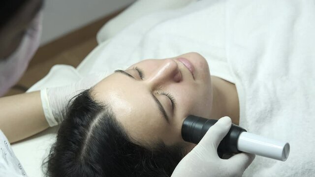 Young woman having facial microcurrent treatment in beauty salon. Beautician using electrical impulses for facial procedure to help serum absorb deep in skin. Healthcare, wellness and medicine