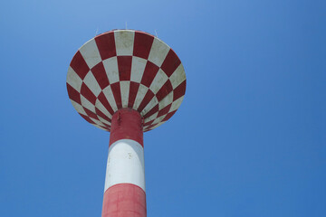 Red and white old water tower rising in the blue sky