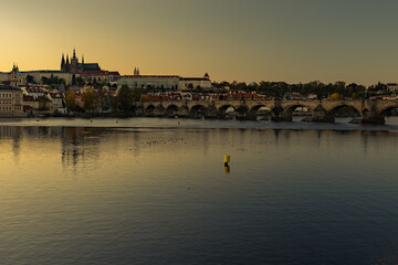 view of the Vltava river and Prague Castle St. Vitus Cathedral and Charles Bridge in the center of Prague at sunset. there are reflections on the river surface and the sky is illuminated by the sun