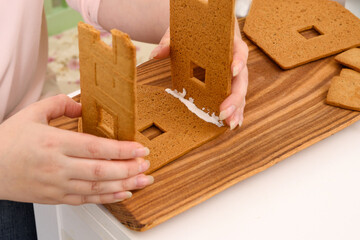 Mom glues the details gingerbread house with protein cream. female hands hold details close-up