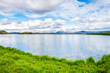 Obraz na płótnie Canvas Landscape water view of Iceland in Skutustadagigar with lake Myvatn during cloudy day and green grass with calm water and mountain in summer