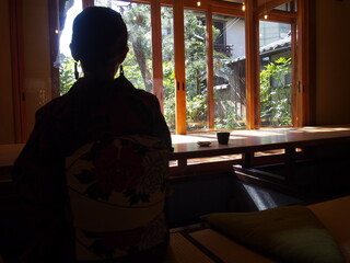 An Asian woman wearing a traditional Japanese kimono is sitting in a Japanese-style restaurant looking at the garden, Kyoto, Japan