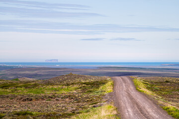 Fototapeta premium View of Blonduos cityscape west of Akureyri with blue sky during summer day and dirt road leading to ocean and water in horizon in Iceland