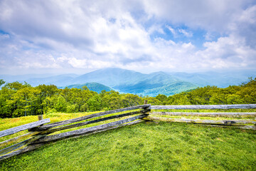 Fototapeta na wymiar Devil's Knob Overlook with fence and green grass field meadow at Wintergreen resort town village in Blue Ridge mountains in summer clouds mist fog