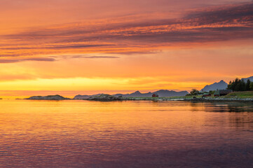 Fototapeta na wymiar Colourful sunset over Norwegian fjords in Lofoten islands with classic red wooden shed in background.