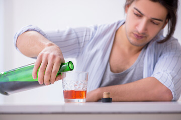 Young male alcoholic drinking whiskey at home