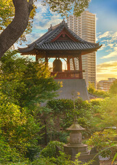 Sunset on the Shōrō bell at the foot of Daibutsu Mount in Ueno Park known as Time Bell of Kaneiji Temple made famous by Matsuo Basho with skyscraper in background.