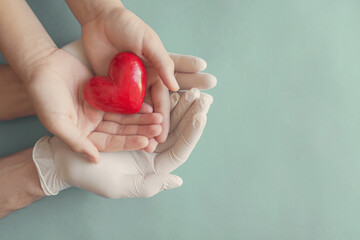 Doctor hands with medical gloves holding child hands and red heart, health insurance and donation concept