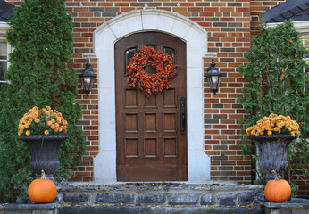 wooden front door of brick house with fall decorative wreath and pumpkins © Spiroview Inc.