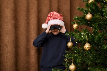  A boy with compressed lips, impatiently, in a striped cap, looks out through the binoculars of...