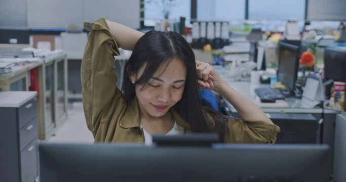 Asian women relax from hard work in office.Office worker raise arm in front of laptop computer on desk.A desk that looks messy.Fatigue from work.