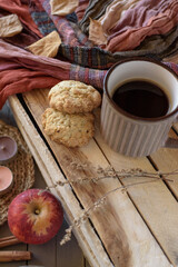 Obraz na płótnie Canvas Oatmeal cookies with a mug of black coffee on a wooden box with dried flowers, an apple, candles, an orange-brown scarf