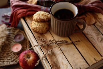 Obraz na płótnie Canvas Oatmeal cookies with a mug of black coffee on a wooden box with dried flowers, an apple, candles, an orange-brown scarf