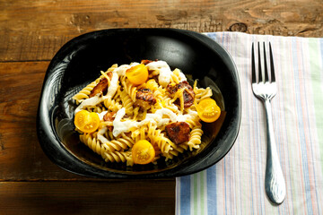 Pasta with chicken and cheese in a black plate on a wooden table on a napkin with a fork.