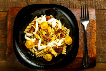 Pasta with chicken and cheese in a black plate on a wooden stand with a fork.