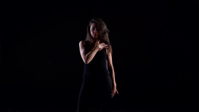 a young energetic woman in a black suit in a Studio on a black background dancing, moving and posing.