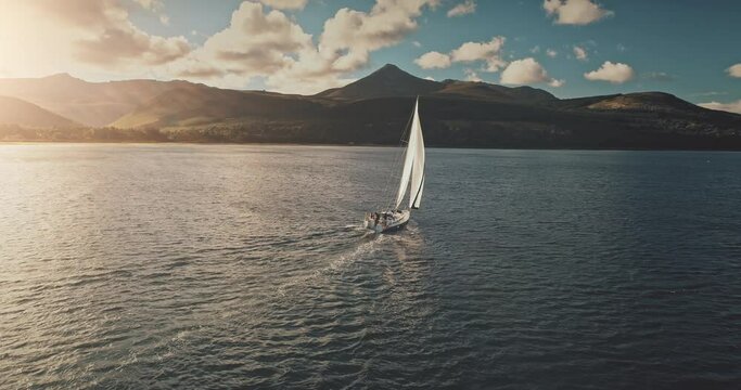 Yacht in bright sunlight sailing at open sea bay aerial. Luxury sailboat cruise at Brodick Pier, Arran Island, Scotland. Cinematic mountain isle on ocean shore admist serene seascape with lonely ship