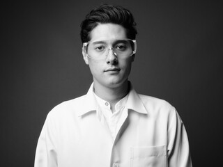 Portrait of young handsome man doctor as scientist with protective glasses