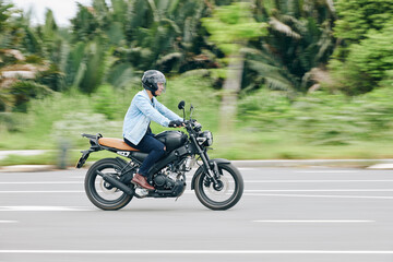 Serious Vietnamese man riding fast on motorcycle, blurred motion in background