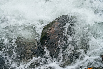 Obraz premium Full frame nature background with boulders in water riffle of mountain river. Powerful water stream of mountain creek. Textured backdrop of fast flow of mountain brook with rapids. Big stones close-up