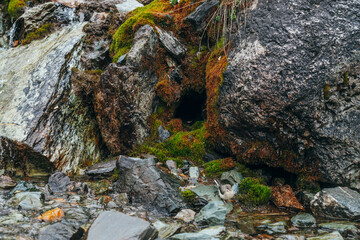 Hole in mossy rock close-up. Scenic rocky background with small cave in boulders with thick moss. Mountain creek on mossy rocks with fresh greenery. Colorful backdrop with rich alpine flora.