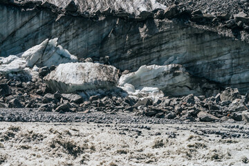 Natural texture of big glacial wall with crevasses close-up. Atmospheric nature background with ice boulders near icy broken wall with cracks. Big peace of ice and stones near surface of glacier.