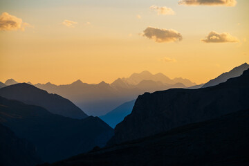 Colorful dawn landscape with beautiful blue mountains silhouettes and golden gradient sky with clouds. Vivid mountain scenery with picturesque multicolor sunset. Scenic sunrise view to mountain range.