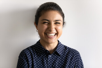 Close up portrait of smiling millennial Indian female isolated on grey studio background laugh at funny joke. Overjoyed happy young mixed race ethnicity woman have fun feel excited. Humor concept.