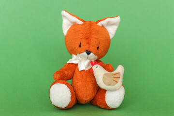 Soft toy ginger fox with chicken on a green background.