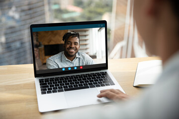 Fototapeta na wymiar Close up rear view of woman look at laptop screen speak talk on video call with smiling African American male friend or colleague. Person have webcam virtual digital conference with ethnic man online.