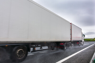 Mega trailer or road train circulating on a day with bad weather due to rain, with the road wet and the wheels raising a cloud of water.