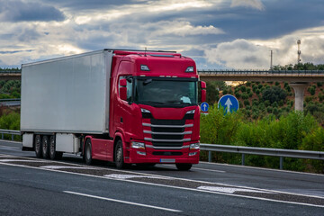 Refrigerated semi-trailer truck driving on a highway under a dramatic sunset sky.