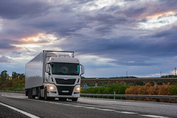 Refrigerated semi-trailer truck driving on a highway under a dramatic sunset sky.