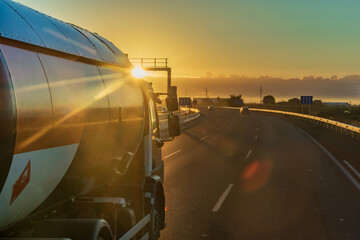 Tank truck for the transport of flammable gases driving on a highway at dawn with the sun in front.