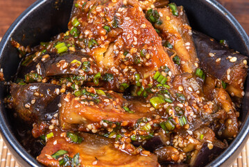 Korean style spicy eggplant salad with spicy sauce and sesame seeds in a large bowl and chopsticks on a bamboo napkin on a rustic wooden table, top view, close-up