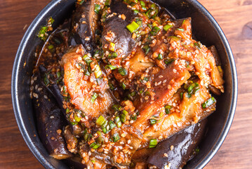Korean style spicy eggplant salad with spicy sauce and sesame seeds in a bowl on a rustic wooden table, top view, close-up
