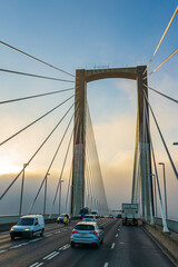 Vehicles driving over a bridge with a bank of fog in the background.