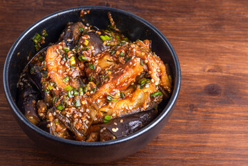 Korean style spicy eggplant salad with spicy sauce and sesame seeds in a bowl on a rustic wooden table, top view, close-up, copy space
