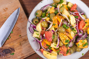 Cooking Italian potato calabrese salad - a bowl of boiled potatoes, tomatoes, onions and olives on a table with a cutting board and a knife