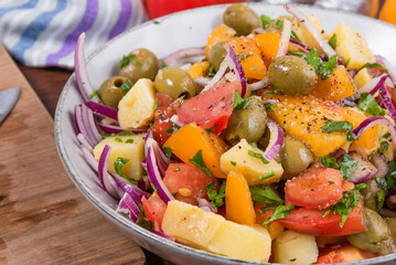 Traditional Italian Calabrian potato salad - a bowl with boiled potatoes, tomatoes, onions and olives on a plain table close-up