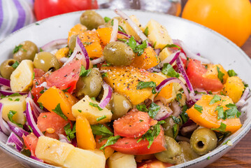 Traditional Italian Calabrian potato salad - a bowl with boiled potatoes, tomatoes, onions and olives on a plain table close-up