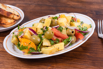 Traditional Italian Calabrian potato salad - oval plate with boiled potatoes, tomatoes, onions and olives on a plain table close-up