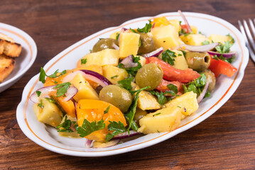 Traditional Italian Calabrian potato salad - oval plate with boiled potatoes, tomatoes, onions and olives on a plain table close-up