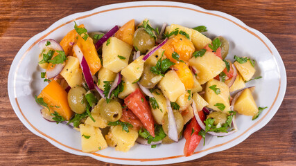 Traditional Italian Calabrian potato salad - oval plate with boiled potatoes, tomatoes, onions and olives on a plain table close-up, top view