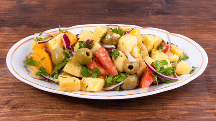 Traditional Italian Calabrian potato salad - oval plate with boiled potatoes, tomatoes, onions and olives on a plain table close-up